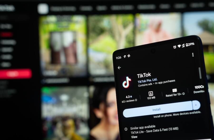 Smartphone screen displaying TikTok app installation page with background showing blurred streaming service interface.